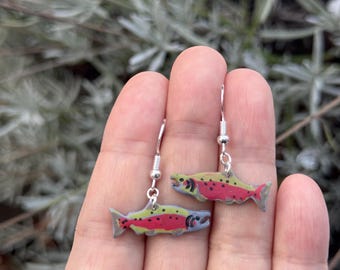 May include: A pair of silver dangle earrings with a salmon fish charm. The salmon is painted with realistic details, including red, yellow, and black spots.