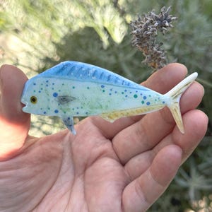 May include: A hand-painted glass figurine of a blue and yellow mahi-mahi fish with green and blue spots. The fish is about 5 inches long and has a realistic appearance.