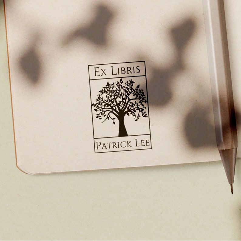 May include: A black and white "Ex Libris" stamp with a tree design and the name "PATRICK LEE" printed below. The stamp is on a cream-colored page with a pen in the background. The image is well-lit, with shadows.