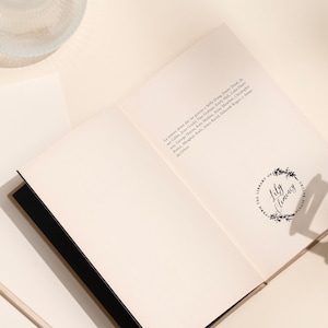 May include: An open book with a black spine and white pages. The book has a stamp on the right page that says "The Library of Lily Clemons".
