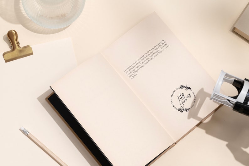 May include: An open book with a black spine and white pages. The book has a stamp on the right page that says "The Library of Lily Clemons".