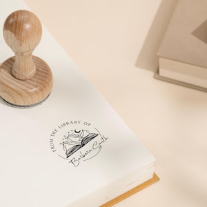 May include: A wooden stamp with a circular design featuring a book with mountains and a crescent moon. The text "From the Library of Barbara Smith" is printed around the design.