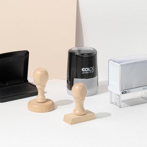 May include: An assortment of office stamps and an ink pad. The stamps include a wooden handle stamp, a rectangular stamp, and a self-inking stamp with the text "COLOR printer R 40". The ink pad is black.
