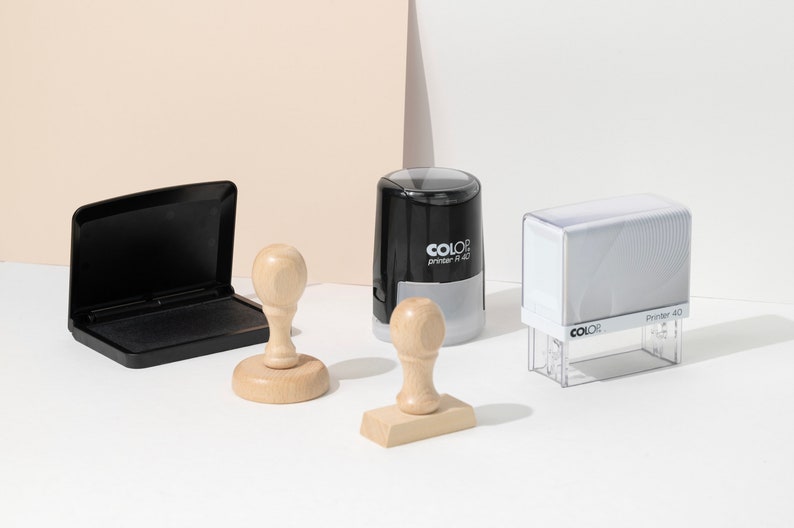 May include: An assortment of office stamps and an ink pad. The stamps include a wooden handle stamp, a rectangular stamp, and a self-inking stamp with the text "COLOR printer R 40". The ink pad is black.