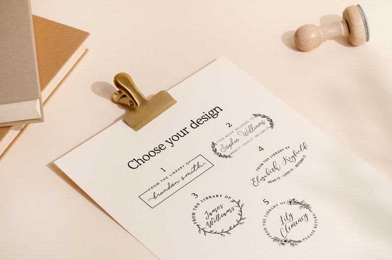 May include: A sheet of paper with the text "Choose your design" and five stamp design options. A gold clip holds the paper. A wooden stamp is at the top right. Books are in the top left.