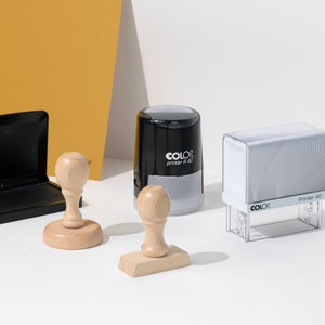 May include: An assortment of office stamps and an ink pad. The stamps include a wooden stamp with a round handle, a rectangular wooden stamp, a black and gray stamp, and a clear stamp with the text "Printer 40".