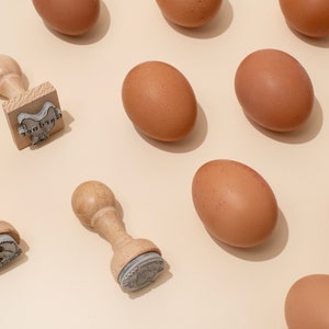 Puede incluir: Una vista cenital de huevos marrones y sellos de madera con el texto "Good Eggs" en uno de los sellos.