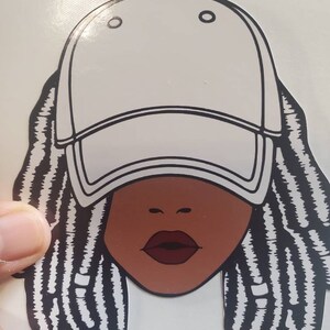 May include: A black and white illustration of a person with dreadlocks wearing a white baseball cap. The person has brown skin and red lips.