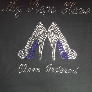 May include: Black t-shirt with silver and blue rhinestones spelling out "My Stepps Have Been Ordered".