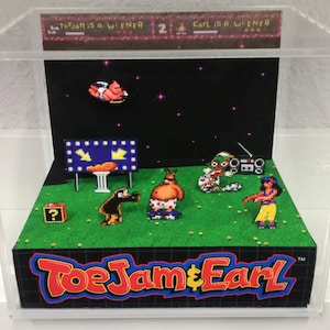 May include: A diorama of the video game ToeJam & Earl, featuring the characters ToeJam and Earl in a 3D environment. The diorama is set against a black background with stars and includes a question mark block, a boombox, and a sign that reads "ToeJam is a Wiener".