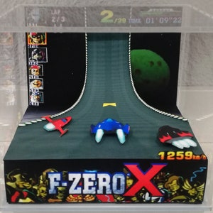 May include: A diorama of the video game F-Zero X, featuring a black, green, and white race track with three spaceships. The spaceships are red, blue, and black. The diorama is in a clear acrylic case. The game's title, "F-ZERO X", is printed on the base of the diorama. The game's logo is red and white. The diorama also includes a small, green planet in the background.