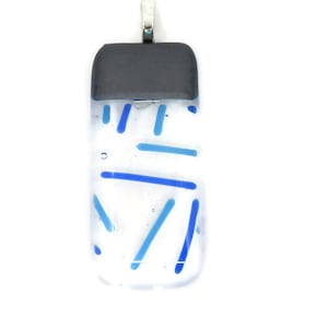 Puede incluir: Colgante rectangular con cuerpo de vidrio transparente, con diseños lineales azules y celeste. La sección superior es de color gris oscuro y tiene una fianza plateada para colgar. El colgante está sobre un fondo blanco.