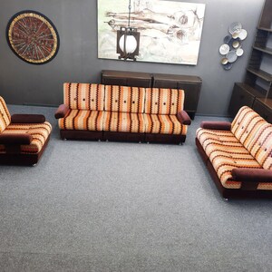 May include: A living room furniture set consisting of a three-seat sofa, a two-seat sofa, and an armchair. Each piece features a striped fabric pattern in shades of orange, yellow, and brown, with dark brown solid-colored armrests and base.