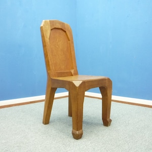 Könnte beinhalten: Ein Holzstuhl mit geometrischem Design. Der Stuhl hat eine hohe Rückenlehne und eine leicht gewölbte Sitzfläche. Der Stuhl ist aus massivem Holz gefertigt und hat eine natürliche Oberfläche.