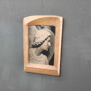 Peut inclure: Une sculpture en relief en niveaux de gris encadrée, représentant un profil humain, dans un cadre en bois clair. Le cadre a un dessus incurvé unique. La sculpture représente une figure classique avec des cheveux et des vêtements détaillés.