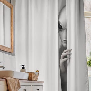 Könnte beinhalten: Schwarz-weißer Duschvorhang mit einem Alien, das hinter dem Vorhang hervorlugt. Der Außerirdische hat große Augen und eine schlanke Hand. Der Vorhang ist weiß und hängt in einem Badezimmer.