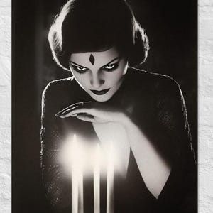 Puede incluir: Un retrato en blanco y negro de una persona con cabello oscuro y una marca en forma de diamante en la frente, inclinada sobre tres velas encendidas. La persona viste una prenda oscura con textura de encaje y maquillaje oscuro en ojos y labios.