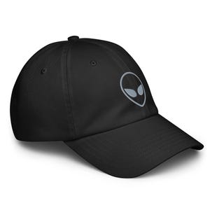 Può includere: Un cappellino da baseball nero con un'icona di testa aliena ricamata in grigio chiaro al centro. Il cappellino presenta una corona strutturata, una visiera curva e un bottone sulla parte superiore. Il design è semplice e lineare.