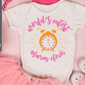 May include: A white onesie with pink text that reads "world's cutest alarm clock" and a yellow alarm clock with pink hearts on the face.