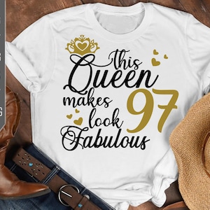 Op de afbeelding: Wit T-shirt met zwarte tekst die "This Queen makes 97 look fabulous" luidt. De tekst is versierd met een gouden kroon en harten.