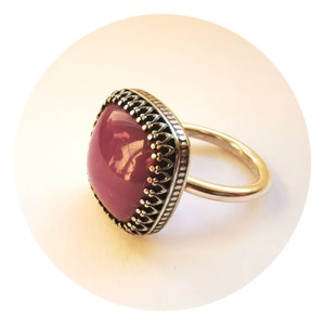 Op de afbeelding: Een zilveren ring met een vierkante, dieppaarse edelsteen gezet in een decoratieve zilveren zetting. De ring heeft een eenvoudige band.