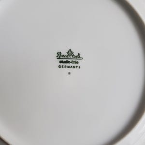 Op de afbeelding: Een witte porseleinen bord met een gebogen rand. Het bord heeft een groen logo met de tekst "Rosenthal studio-linie GERMANY" en de letter "B". Het bord is schoon en lijkt ongebruikt.