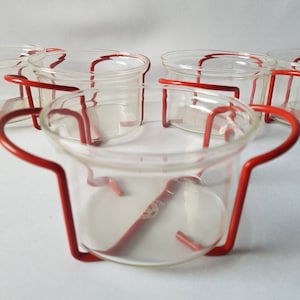 Puede incluir: Conjunto de seis cuencos de vidrio transparente con soportes de metal rojo. Los cuencos son redondos con un borde ligeramente ensanchado. Los soportes de metal rojo tienen un diseño simple y curvado, que proporciona un asa y soporte.