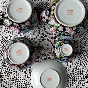 May include: A black porcelain tea set with floral designs in pink, white, blue, and yellow. The set includes a teapot, two teacups, and a saucer. The underside of each piece has text that reads "Made in China".