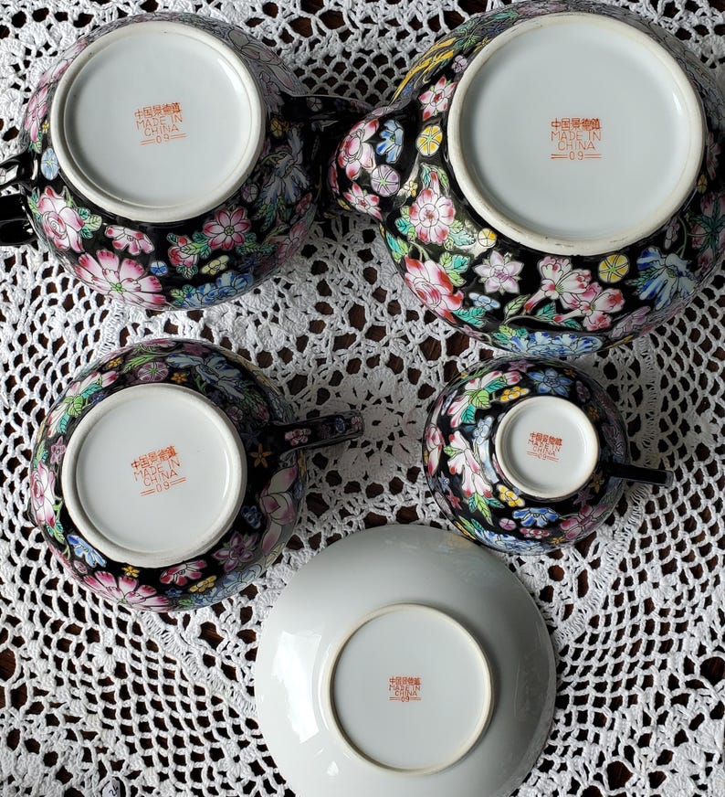 May include: A black porcelain tea set with floral designs in pink, white, blue, and yellow. The set includes a teapot, two teacups, and a saucer. The underside of each piece has text that reads "Made in China".