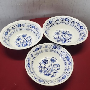 Puede incluir: Tres cuencos de cerámica blanca con un diseño floral azul. Los cuencos tienen un borde festoneado y un patrón azul detallado alrededor del borde y en el centro. El diseño floral presenta flores y hojas estilizadas.