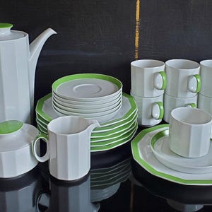 Op de afbeelding: Een wit porseleinen theeservies met een geometrisch ontwerp en groene accenten. De set bevat een theepot, suikerpot, melkkan, kopjes, schotels en borden. De handvatten en randen zijn groen.