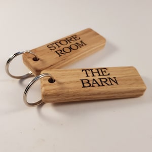 Könnte beinhalten: Zwei Holzschlüsselanhänger mit Metallringen. Ein Schlüsselanhänger sagt "STORE ROOM" und der andere sagt "THE BARN".