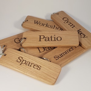 May include: A set of six wooden key tags with engraved labels. The labels read "Workshop", "Patio", "Gym Key", "Spares", "Summer House", and "Dad". Each tag has a metal ring attached.