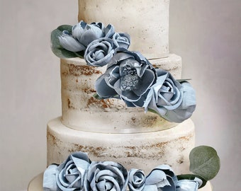 May include: A three-tiered wedding cake with a rustic, white frosting and decorated with light blue flowers. The cake is on a white cake stand.