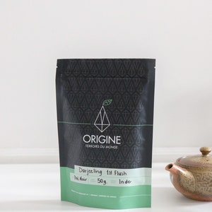 May include: A black pouch with white text that reads "Origine Terroirs du Monde" and "Darjeeling 1st Flush", "The Noir", "50g.", and "Inde".
