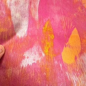 May include: Abstract artwork with a textured appearance. The piece features a blend of pink, orange, and yellow hues, creating a vibrant and dynamic composition. The brushstrokes and color variations add depth and visual interest to the artwork.