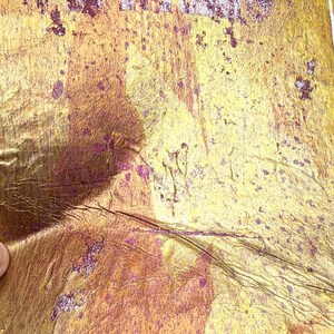 May include: Close-up of textured, metallic gold paper with purple accents. The paper has a distressed appearance with visible creases and imperfections. The overall effect is a vintage or antique aesthetic, suitable for craft projects.