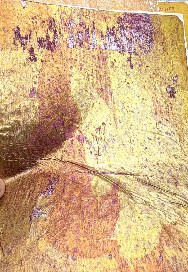 May include: Close-up of textured, metallic gold paper with purple accents. The paper has a distressed appearance with visible creases and imperfections. The overall effect is a vintage or antique aesthetic, suitable for craft projects.