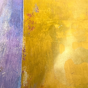 May include: Close-up of a textured surface with a color gradient. The right side is a golden yellow, and the left side is a mix of purple and blue. There are small spots of red and purple along the edge.