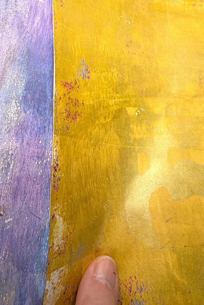 May include: Close-up of a textured surface with a color gradient. The right side is a golden yellow, and the left side is a mix of purple and blue. There are small spots of red and purple along the edge.