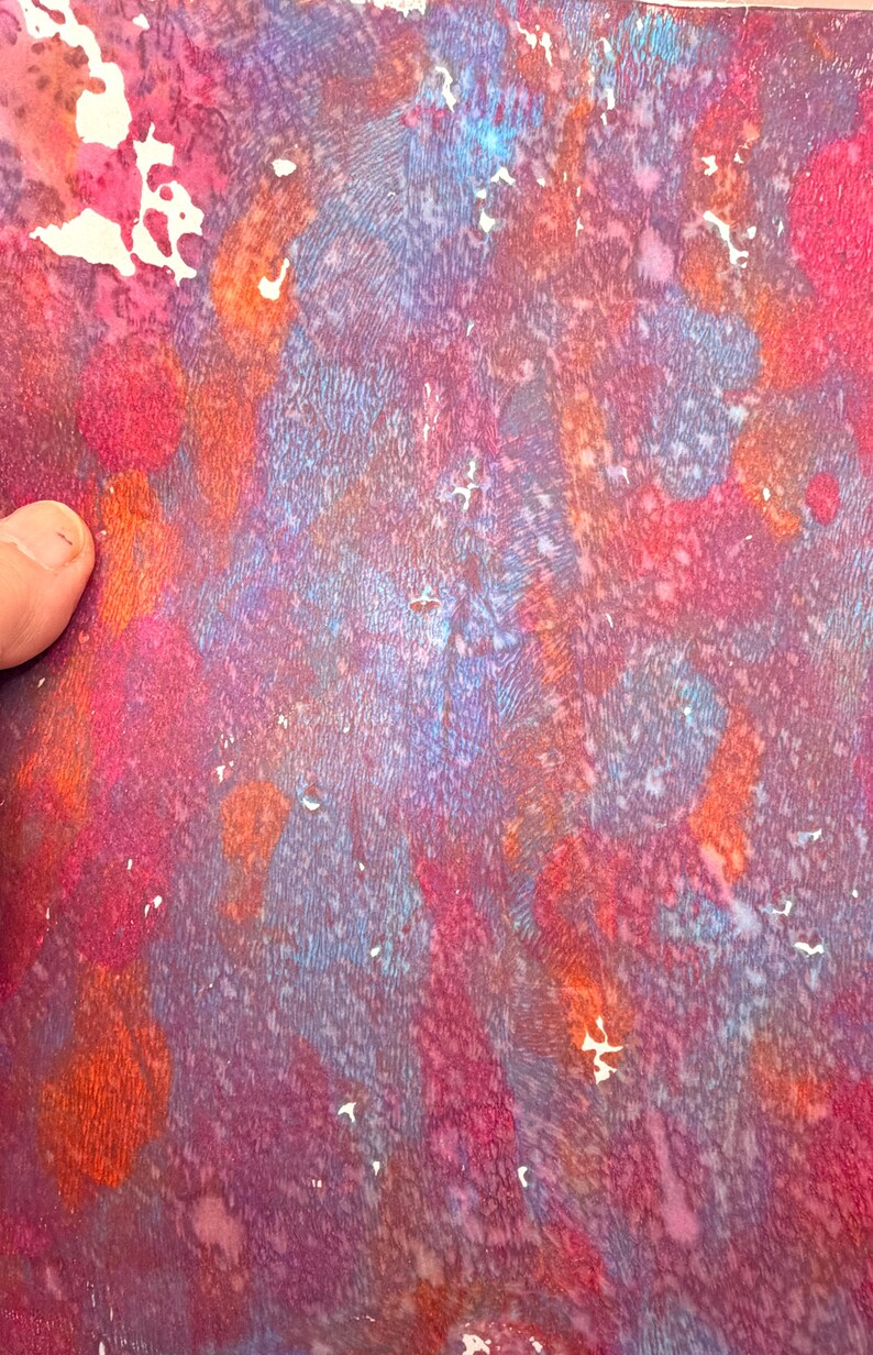 May include: Abstract artwork with a textured surface. The piece features a blend of colors, including shades of red, purple, orange, and blue. The artwork has a watercolor-like appearance with a mix of splatters and streaks.