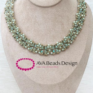 Pode incluir: Um colar delicado de contas verdes e douradas em um expositor. O colar é feito com pequenas contas facetadas e tem um padrão tecido. O texto "AVA Beads Design make your own jewellery" é visível abaixo do colar.