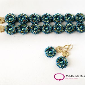 May include: A teal blue beaded bracelet with gold accents and matching earrings. The bracelet has a double row of beads and the earrings are dangle style. The jewelry is made by AVA Beads Design.