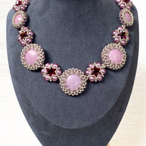 May include: A pink and silver beaded necklace with a pink stone centerpiece. The necklace is displayed on a gray mannequin bust. The text "AVA Beads Design" is visible at the bottom of the image.