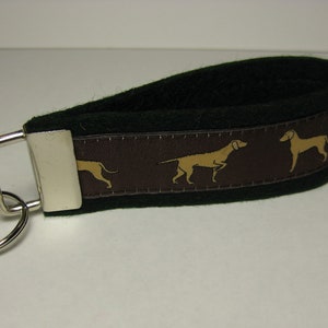 May include: A brown and black key chain with a silver key ring and a brown fabric strap with a repeating pattern of tan dogs.