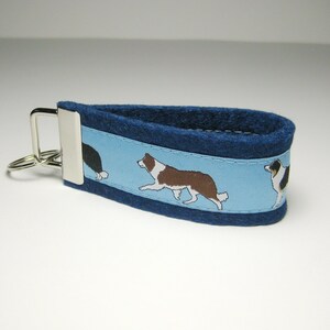 May include: Blue felt keychain with a light blue stripe featuring a repeating pattern of black and white border collies.