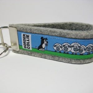 May include: Gray felt keychain with a blue and green ribbon featuring a cartoon border collie herding sheep. The ribbon says "BORDER COLLIE".