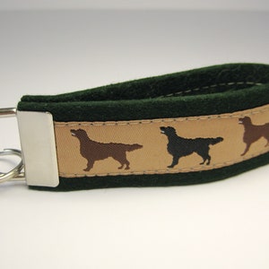 Könnte beinhalten: Grüner und brauner Stoffschlüsselanhänger mit drei gestickten Silhouetten von Golden Retrievern. Der Schlüsselanhänger hat einen silbernen Schlüsselring.
