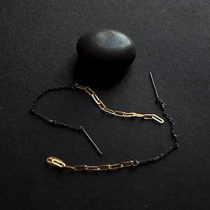 May include: Two pairs of earrings with black and gold chains. One pair has a black chain with a gold chain attached to it. The other pair has a gold chain with a black chain attached to it. The earrings are on a black surface.