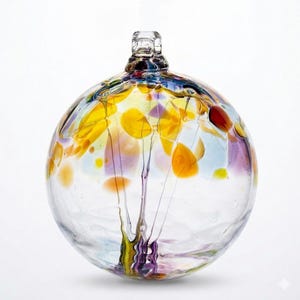 May include: A clear, spherical glass ornament with colorful abstract designs. The ornament features yellow, orange, purple, and red accents, with a tree-like pattern in the center. The top has a small, textured glass loop.